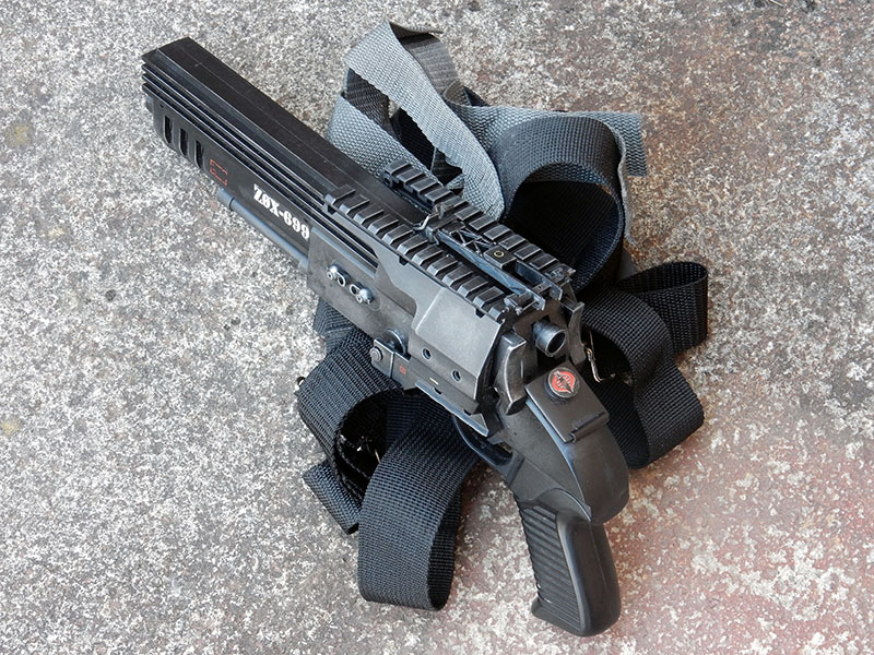Réplique d'arme de cosplay noire avec sangle, posée sur un sol en béton