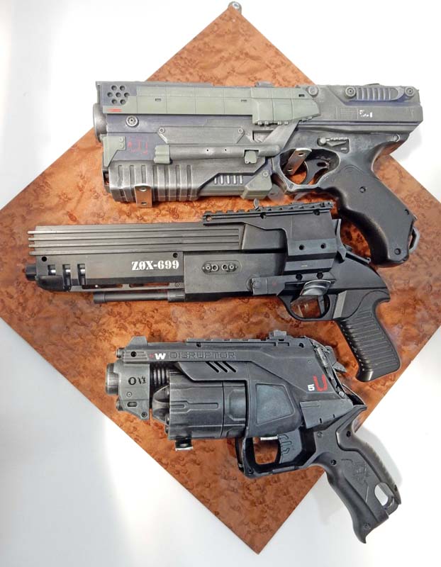 Trois pistolets futuristes de cosplay peints style usé, exposés sur support en bois