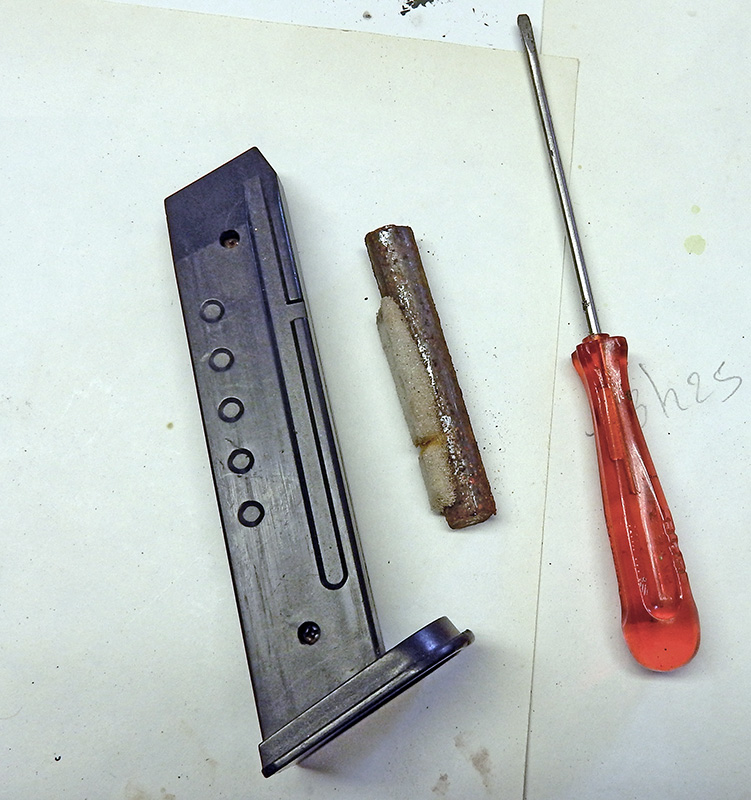 Chargeur de pistolet métallique démonté, ressort rouillé et tournevis à manche rouge posés sur papier