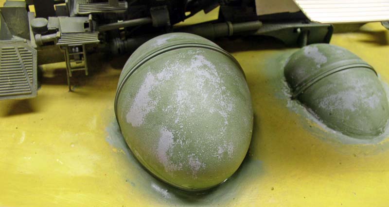 Coques sphériques vert kaki en cours de patine près d'éléments de maquette militaire sur établi jaune