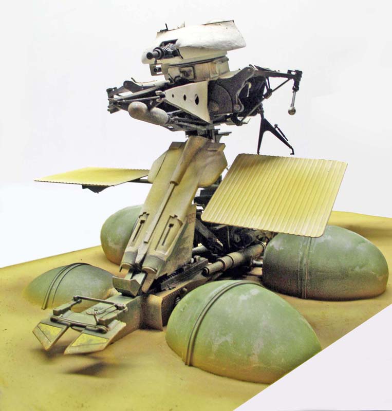 Maquette de droïde de combat science-fiction posé sur un diorama sablonneux avec coupoles vertes