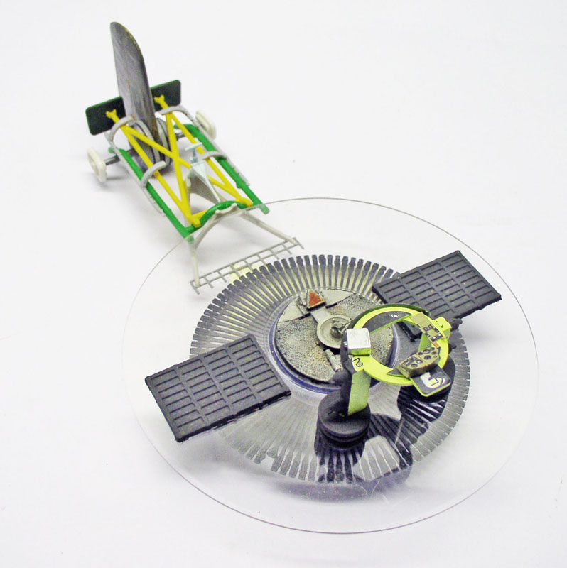 Maquette de satellite aux panneaux solaires sombres et structure jaune et verte en arrière-plan