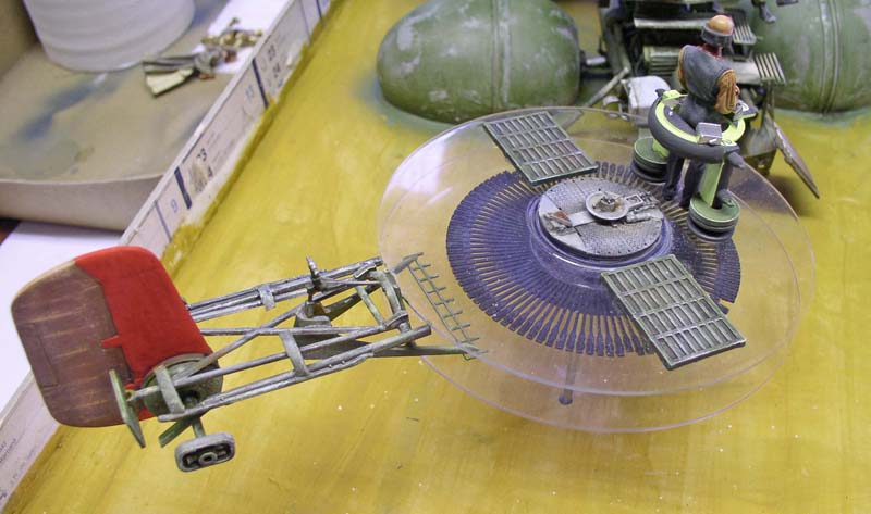 Maquette de podracer en construction avec figurine de pilote sur établi de modélisme