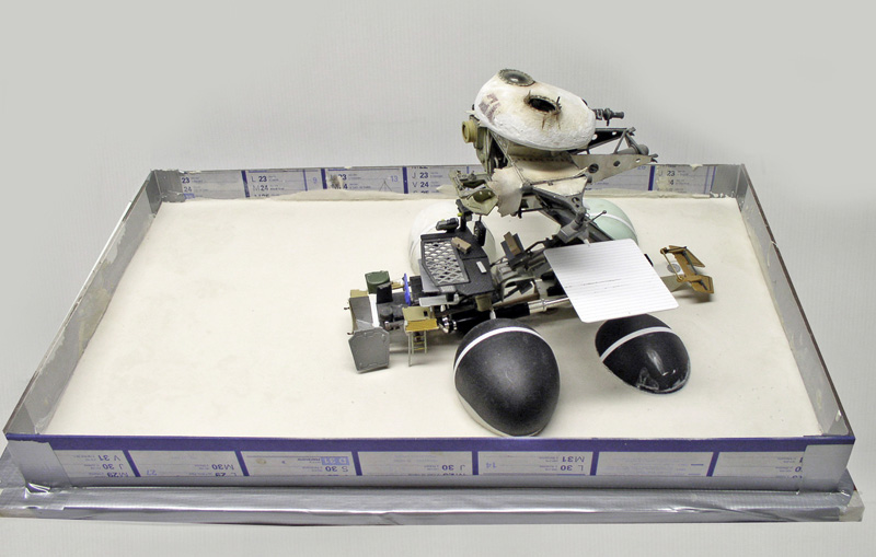 Maquette de robot droïde en construction sur socle blanc avec grandes sphères noires