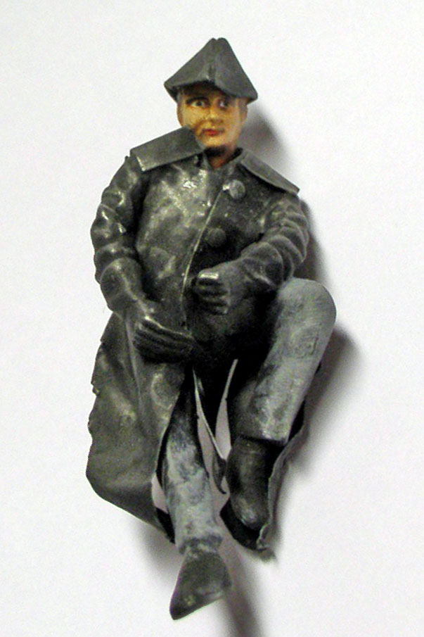 Figurine de soldat en manteau gris et calot, peinte, position assise sur fond blanc