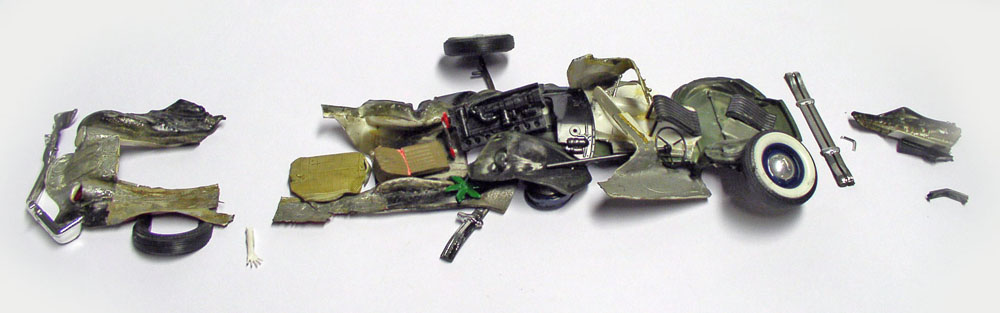 Maquette de voiture détruite, carrosserie déchiquetée et pièces éparpillées sur fond blanc
