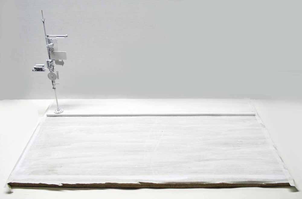 Pièce de maquette gris métallisé montée sur support, posée sur socle blanc en préparation