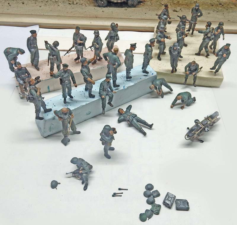 Nombreuses figurines de soldats peintes en gris et accessoires miniatures disposés sur un établi