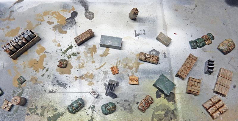 Accessoires miniatures peints pour locomotive BR52 : caisses, ballots et chargements disposés sur plan de travail