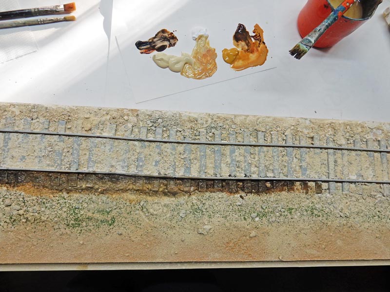 Voie ferrée miniature patinée sur diorama avec pinceaux et palette de peintures pour la patine