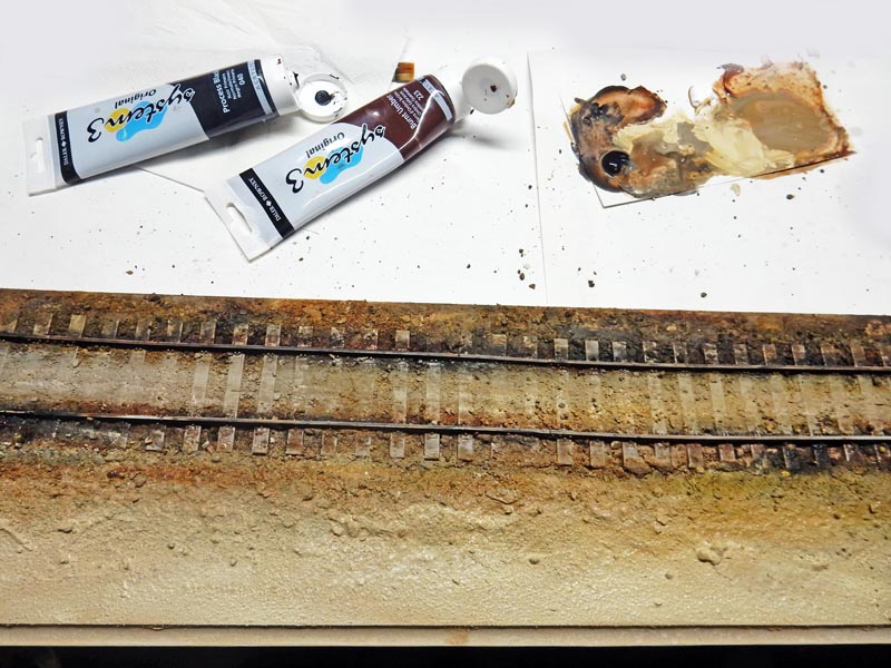 Tubes de peinture acrylique et palette près d'une voie ferrée miniature patinée en cours de vieillissement