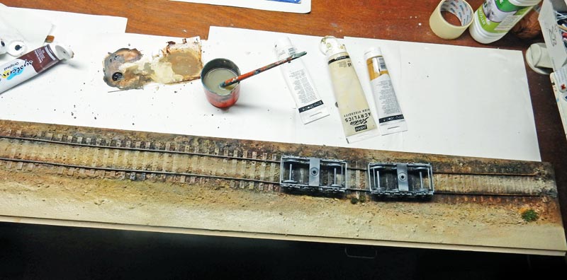 Patine d'une voie ferrée miniature avec tubes de peinture acrylique et châssis de wagons sur l'établi