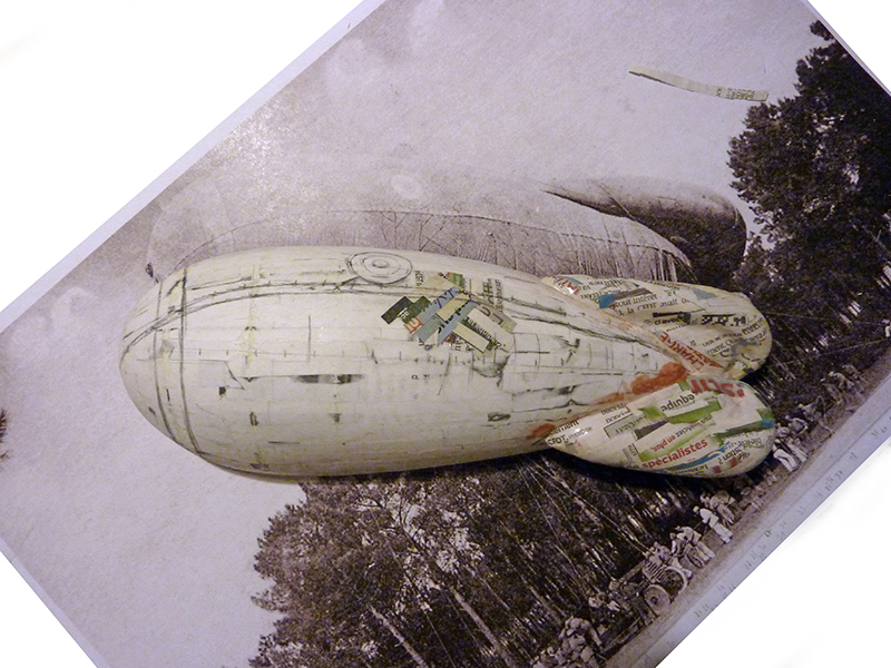 Maquette en papier mâché d'un ballon dirigeable posée sur une photographie ancienne en sépia