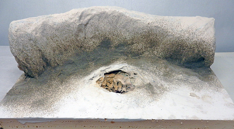 Maquette de diorama montrant une formation rocheuse beige avec cavité centrale sur socle