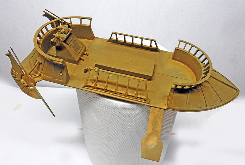 Maquette de la Barge Star en montage, coque ocre avec passerelles et canon antiaérien posée sur un support