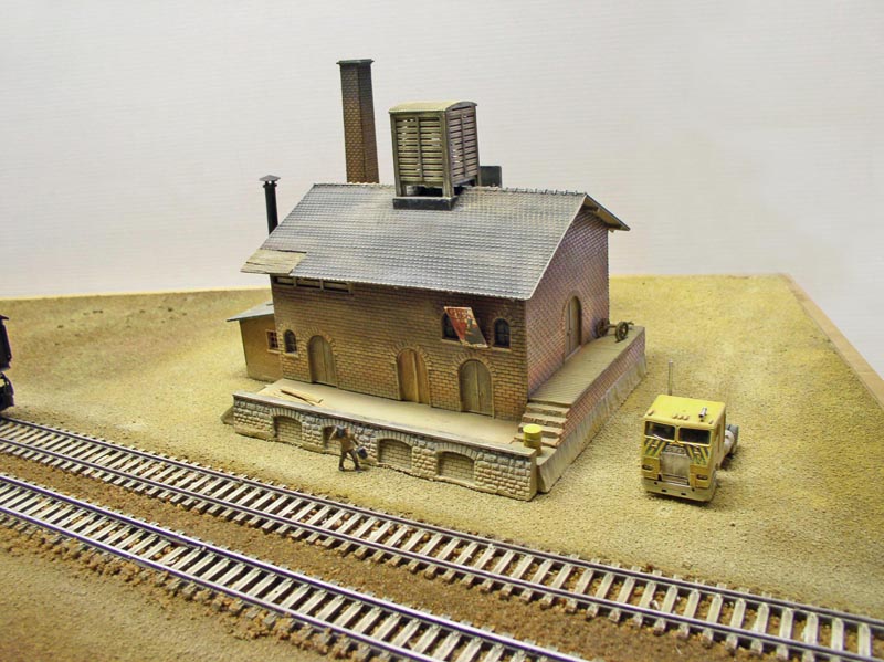 Maquette de bâtiment industriel en briques avec cheminée, voies ferrées et camion miniature