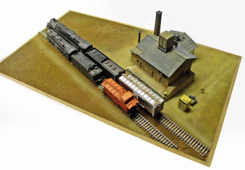 Maquette de locomotive à vapeur Big Boy avec wagons et bâtiment industriel sur diorama ferroviaire