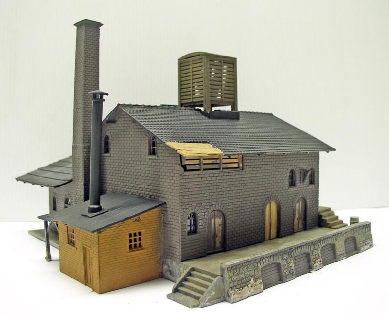 Maquette d'un bâtiment industriel en briques grises avec haute cheminée, château d'eau et escaliers