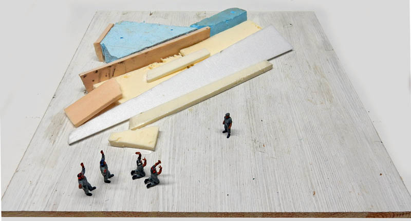 Blocs de mousse et polystyrène posés sur une planche, avec figurines pour l'échelle