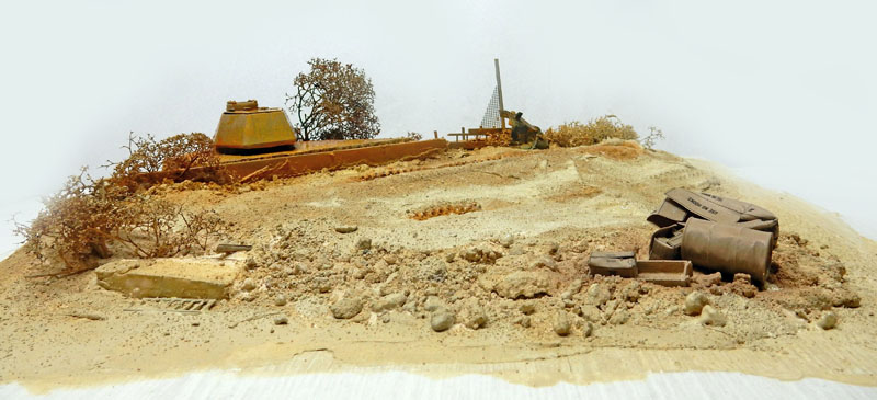 Diorama désertique avec tourelle de char enterrée, bidons rouillés et végétation sèche