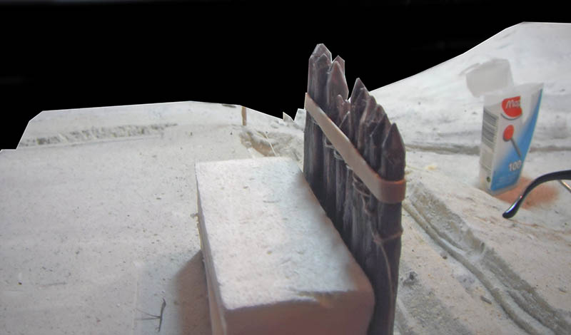 Pieux de palissade en bois taillés et serrés par un élastique sur maquette de terrain