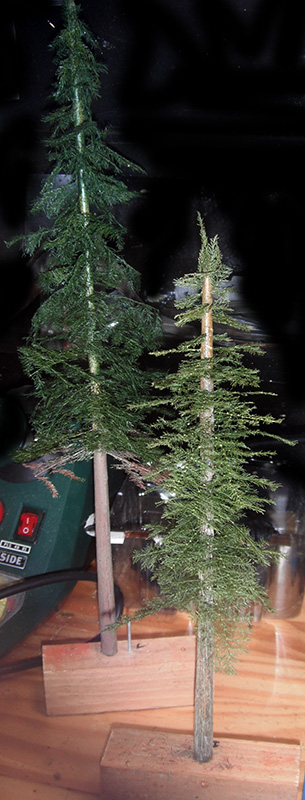 Deux sapins miniatures en cours de fabrication sur socles en bois pour maquette
