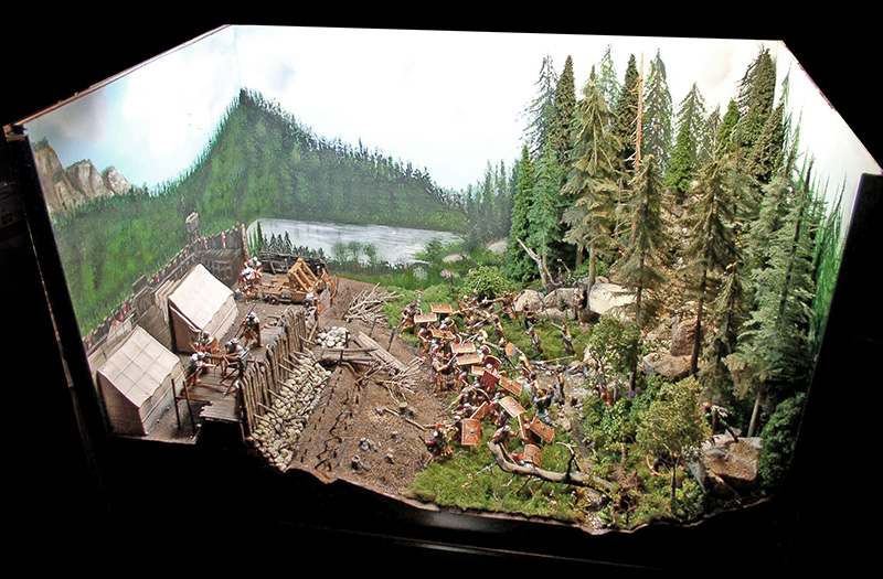 Diorama de camp romain assiégé près d'un lac, soldats attaquant une palissade en forêt