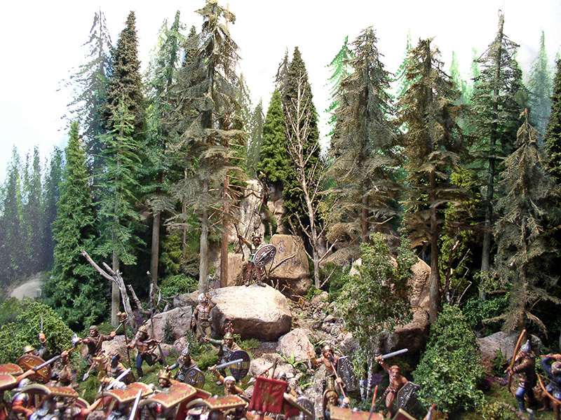 Diorama de soldats romains attaquant dans une forêt de sapins entre rochers