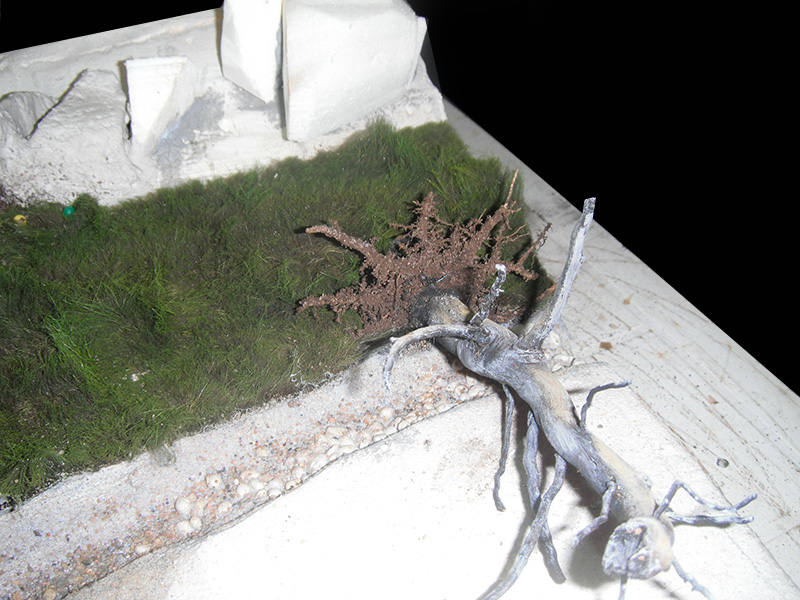 Maquette de camp romain en construction avec talus herbeux, arbre miniature et chemin de gravier