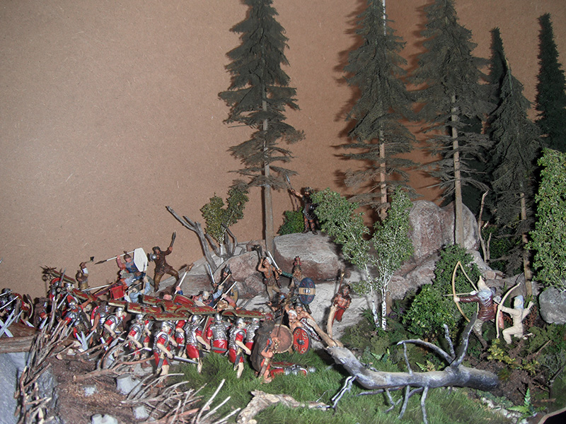 Diorama de figurines représentant une bataille entre légionnaires romains et guerriers dans une forêt de sapins