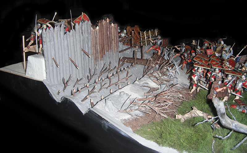 Maquette de camp romain avec palissade défensive en bois et figurines de légionnaires assaillant le rempart