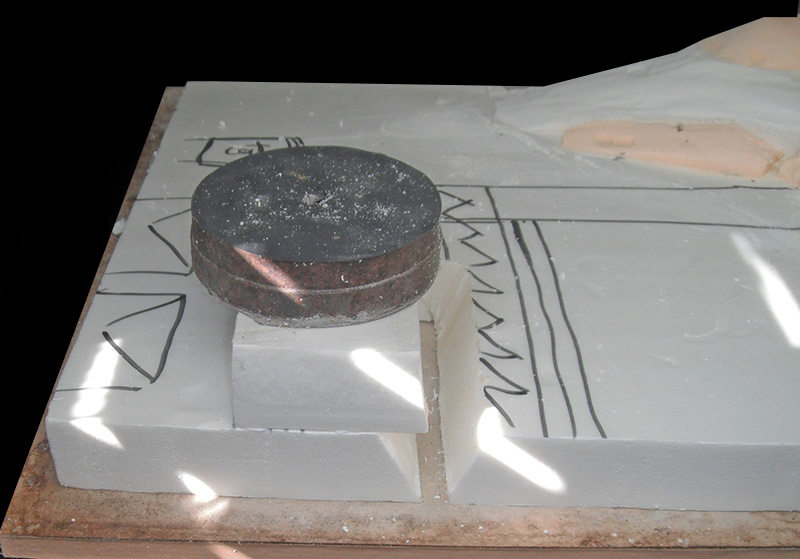 Poids métallique maintenant un bloc de polystyrène collé sur la maquette du camp romain en construction