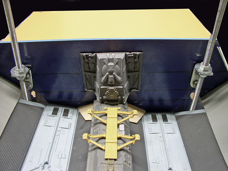 Maquette de cargo spatial en construction avec structure jaune centrale et tiges filetées de maintien