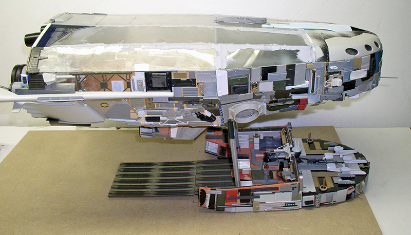 Maquette de cargo spatial argenté en construction, coque détaillée et section moteur posées sur l'établi