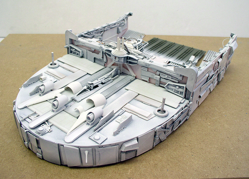 Maquette de cargo spatial gris en construction avec détails de surface et tuyères posée sur établi