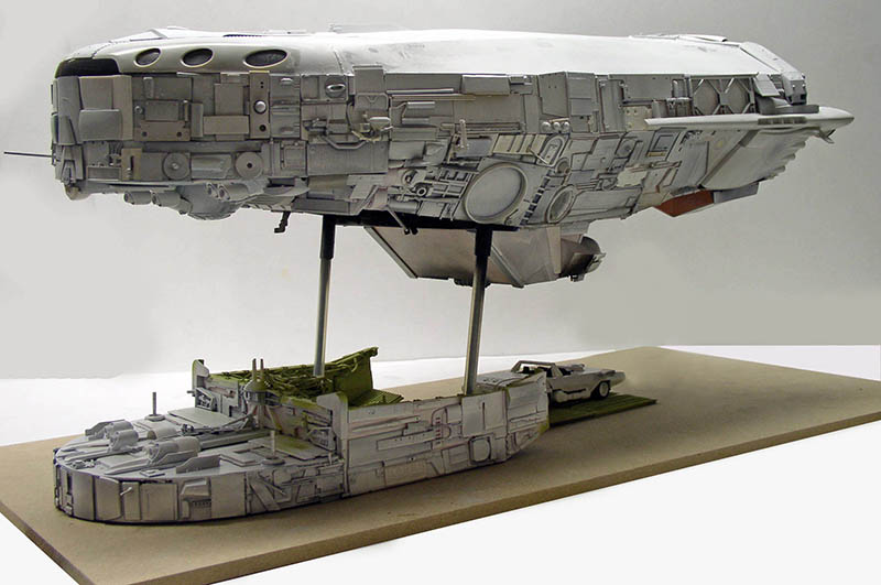 Maquette de cargo spatial gris sur supports au-dessus d'un diorama détaillé avec navette