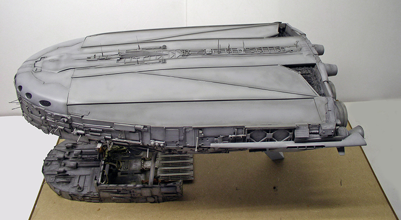 Maquette de cargo spatial gris en cours de montage posée sur un socle en carton