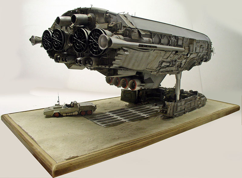 Maquette de cargo spatial gris posé sur un diorama avec véhicule terrestre et plateforme