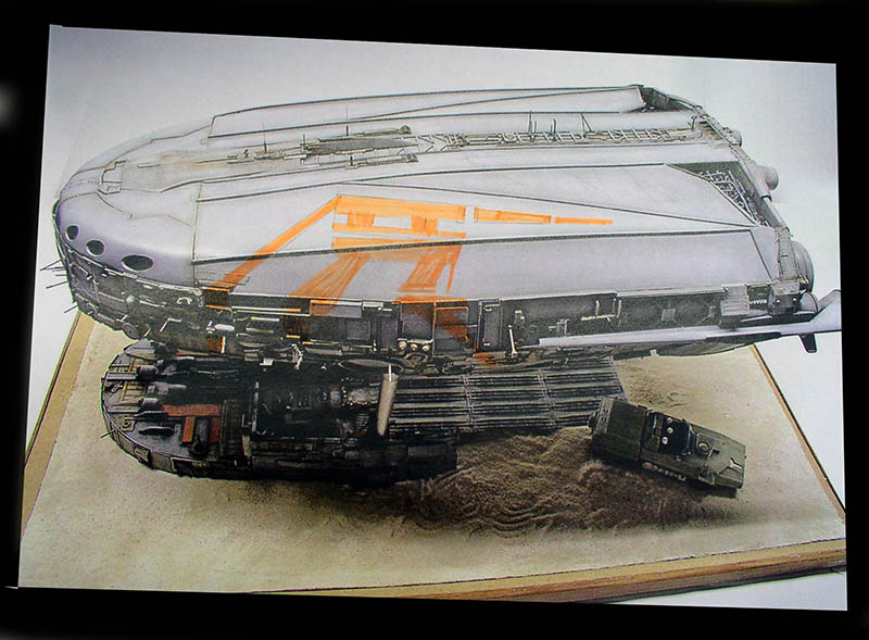 Maquette de cargo spatial gris aux marquages orange posée sur un diorama sableux