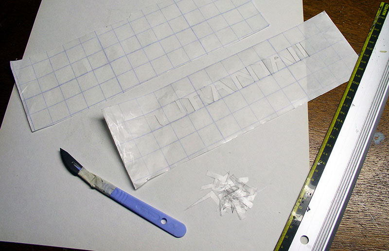 Lettrage découpé dans un film transparent quadrillé avec scalpel et règle métallique