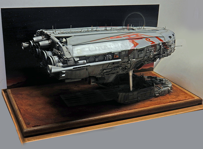 Maquette de cargo spatial gris sur diorama avec socle bois et fond étoilé