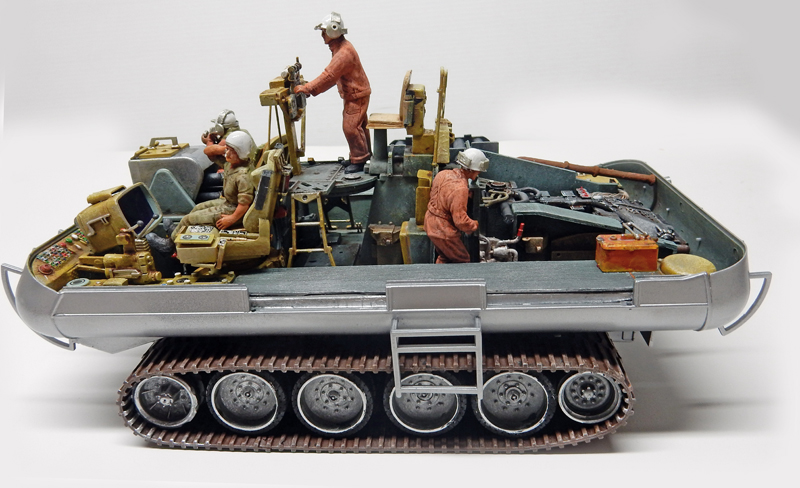 Maquette de châssis chenillé avec figurines de mécaniciens en combinaison travaillant sur le moteur