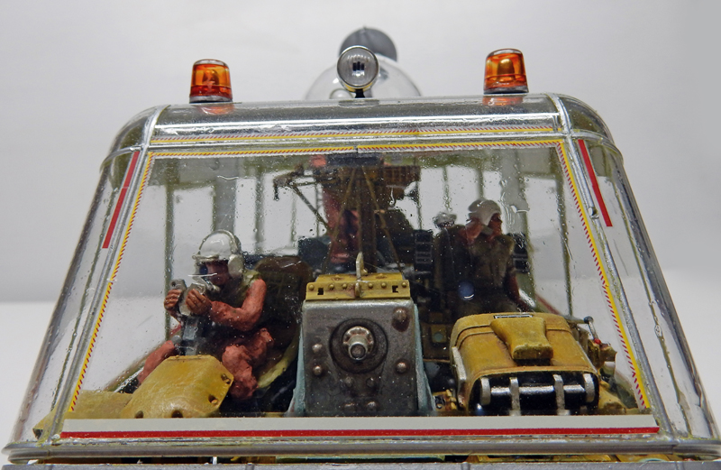 Cabine vitrée de chariot futuriste avec deux figurines casquées et gyrophares orange, diorama de maquettisme