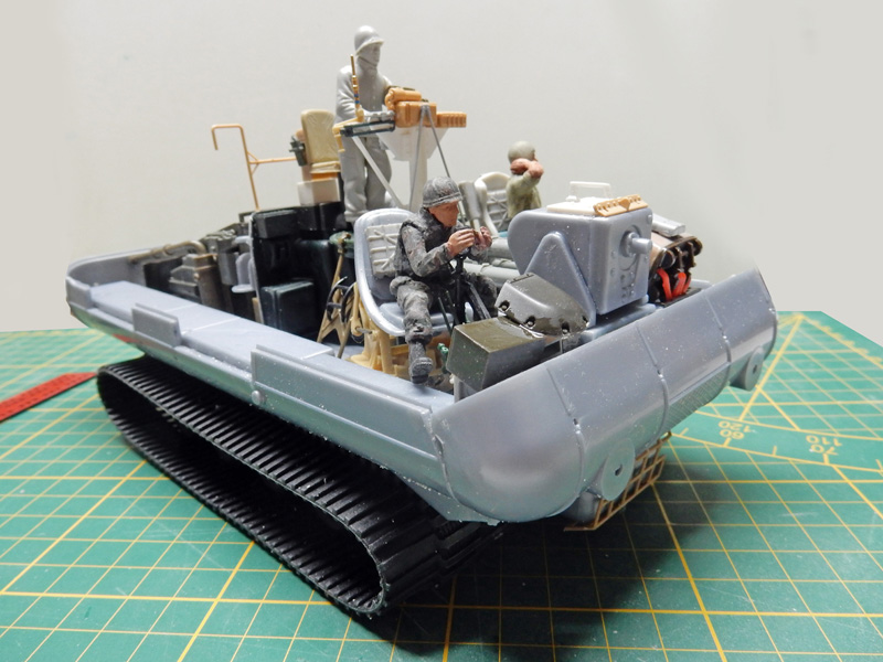 Maquette de véhicule chenillé amphibie gris avec figurines de soldats en cours d'assemblage sur tapis de découpe