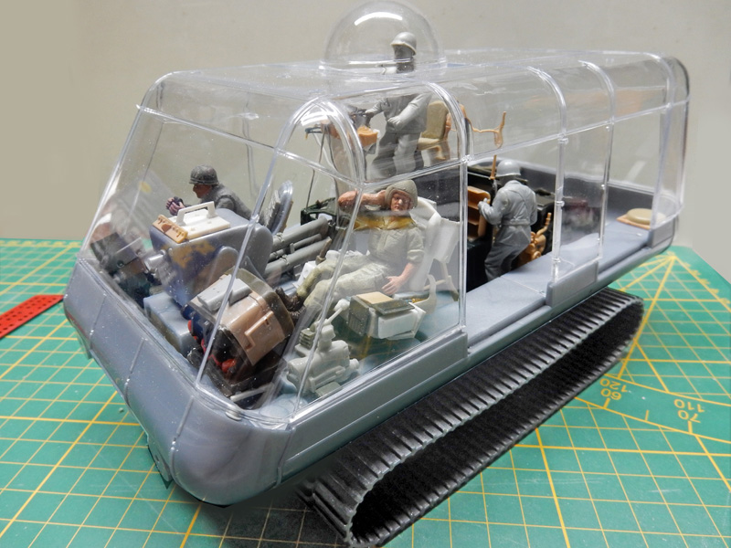 Maquette de véhicule chenillé à habitacle transparent avec figurines, posée sur tapis de découpe
