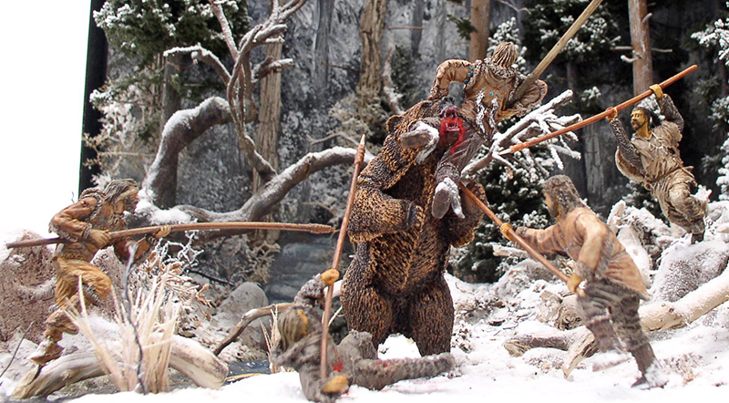 Diorama préhistorique de chasseurs attaquant à la lance un ours dressé dans une forêt enneigée