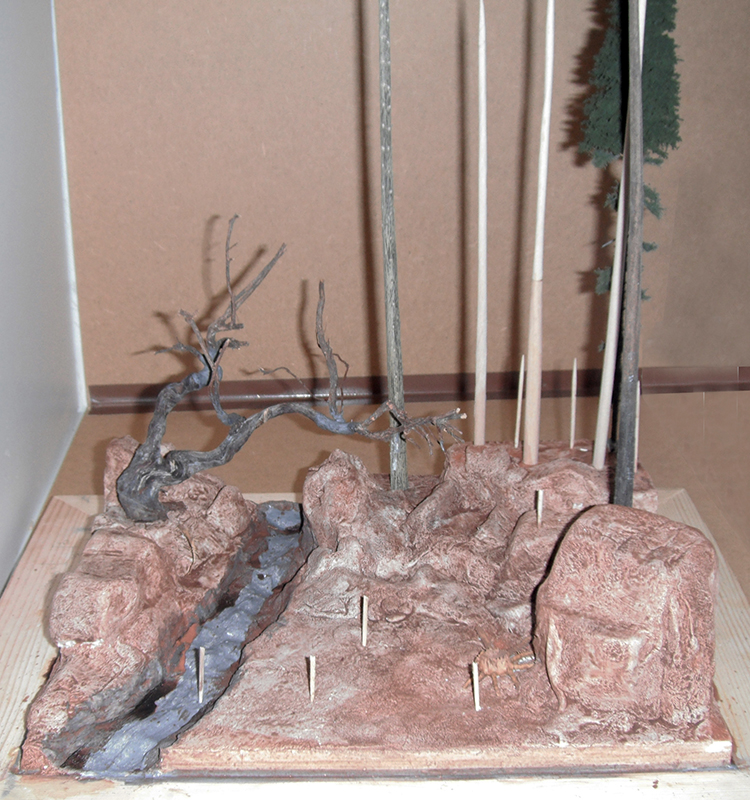 Diorama de maquette en cours avec rochers, ruisseau, arbre mort et troncs d'arbres