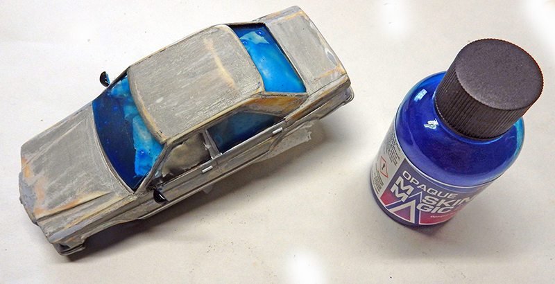 Maquette de voiture grise avec liquide de masquage bleu appliqué sur les vitres, flacon Maskol à côté