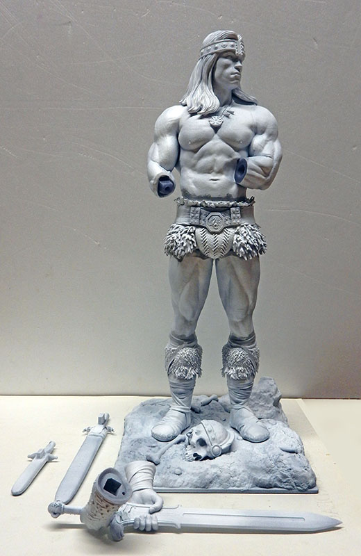 Maquette de Conan en apprêt gris non peinte avec épées et accessoires séparés posés devant le socle
