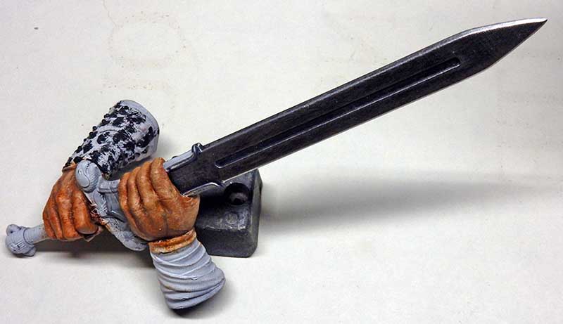 Mains peintes de la figurine Conan tenant une longue épée métallique posée sur socle